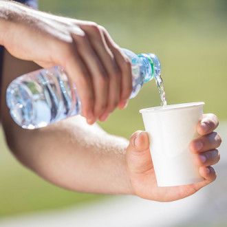 Zwei Hände gießen Wasser aus einer Plastikflasche in einen Pappbecher